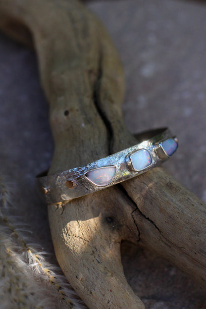 Silver bracelet with opal stones on a wooden surface.