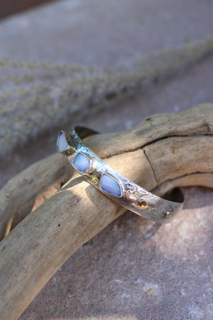 Silver bracelet with opal stones on a piece of driftwood