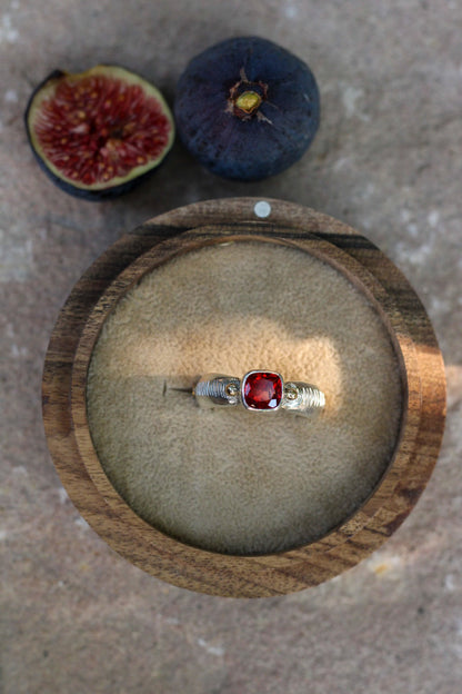 Ring with a red gemstone on a wooden dish with figs in the background