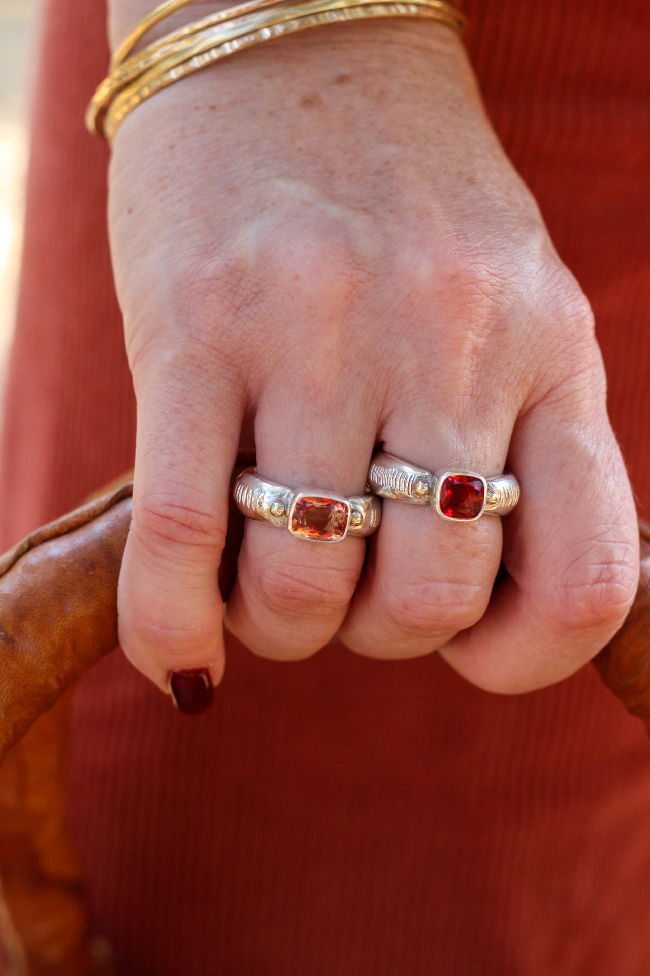 Close-up of a hand wearing two silver rings with red gemstones against a blurred background.