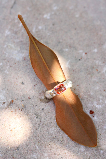 Ring with a red gemstone on a brown leaf against a concrete background