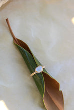 Load image into Gallery viewer, Gold ring with a moonstone on a green leaf against a beige background
