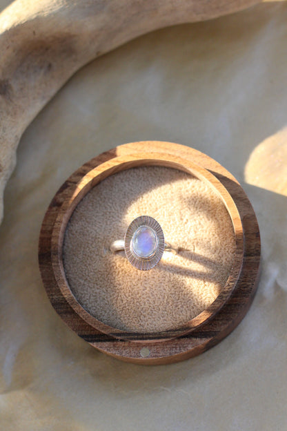 Ring with a moonstone in a wooden box on a stone surface