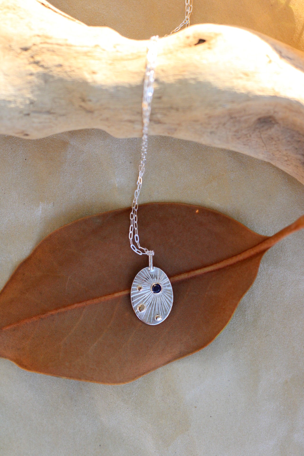 Silver necklace with a pendant on a leaf, the pendant that has a sapphire and small gold accents, on a leaf