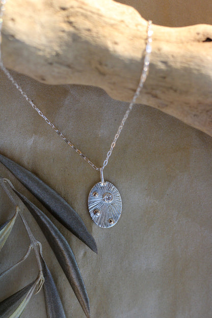 Silver necklace with a pendant by a piece of driftwood, pendant has a diamond and small gold accents.