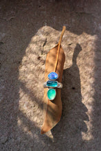 Load image into Gallery viewer, Ring with blue and green gemstones on a brown leaf against a textured brown background
