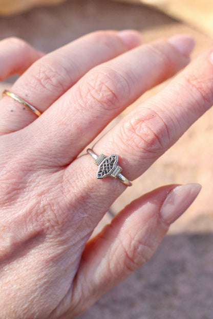 Close-up of a hand wearing a silver ring with a Silver ring with a vintage component  design next to two baguette diamonds on a blurred background