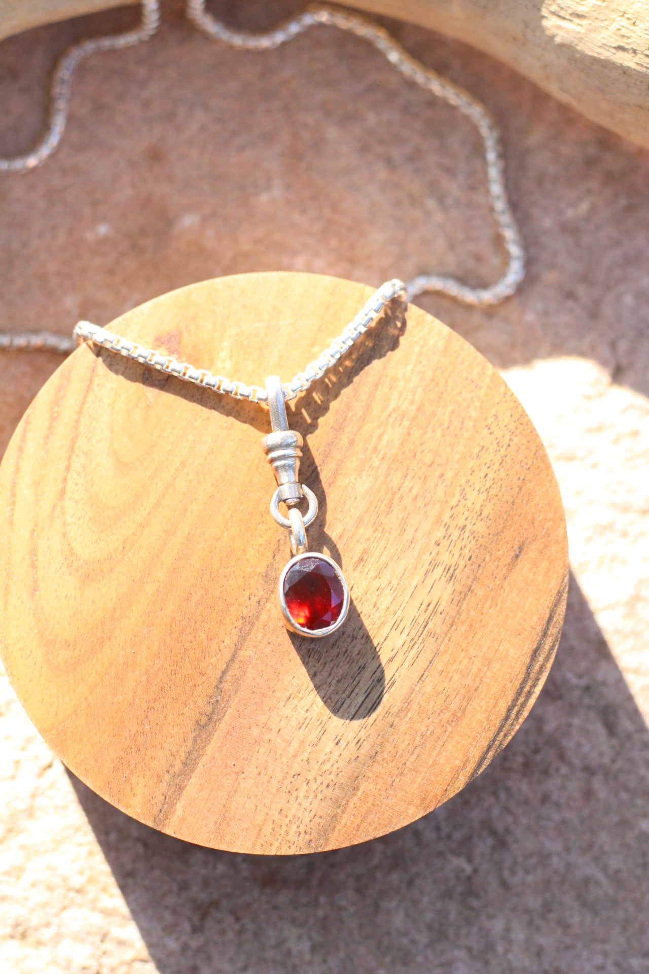 Silver necklace with a red gemstone pendant on a wooden surface