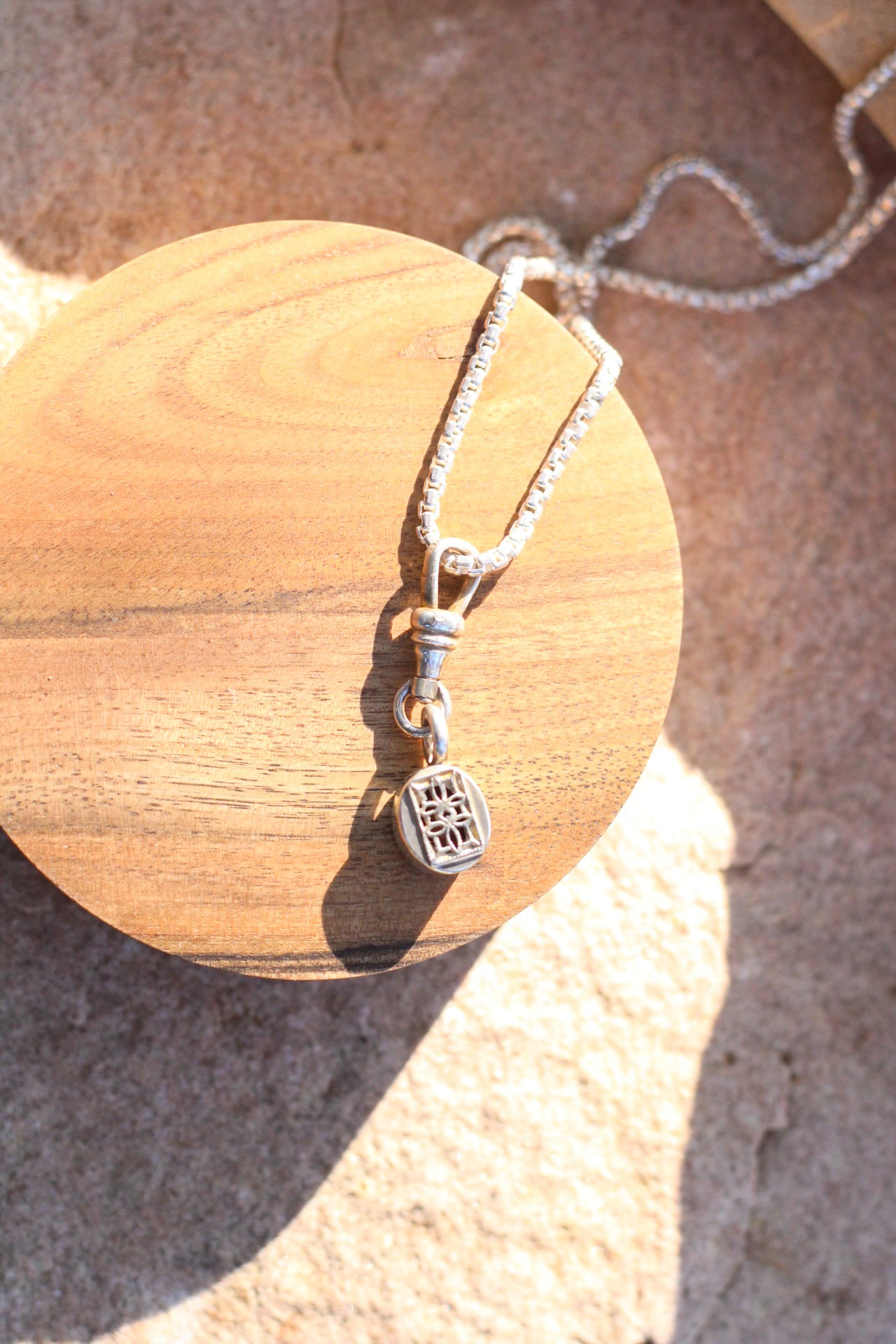 The back of a silver pendant with intricate details with a pendant on a wooden shaped block