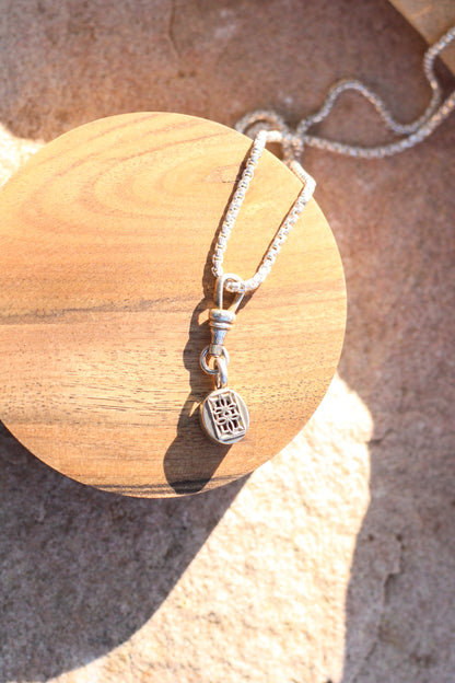 The back of a silver pendant with intricate details with a pendant on a wooden shaped block