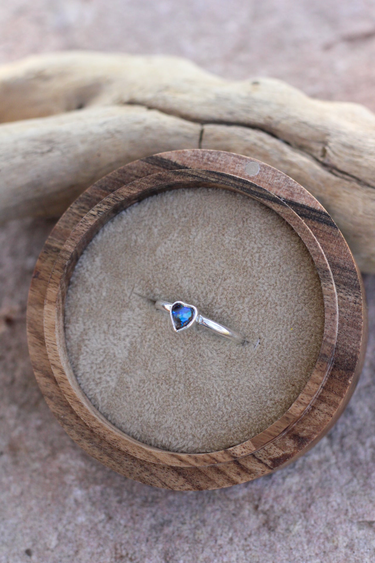 Heart-shaped blue opal gemstone ring on a wooden ring box with a natural background
