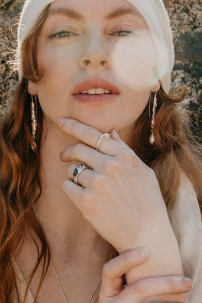 Woman with long hair and silver earrings, and rings, with a blurred background.