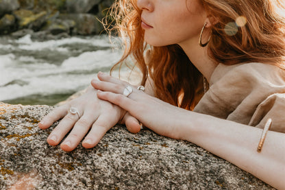 Close-up of a person's hand with rings on a rock by a flowing stream