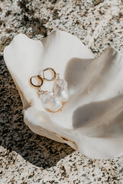 Pearl earrings on a white shell with a textured surface background