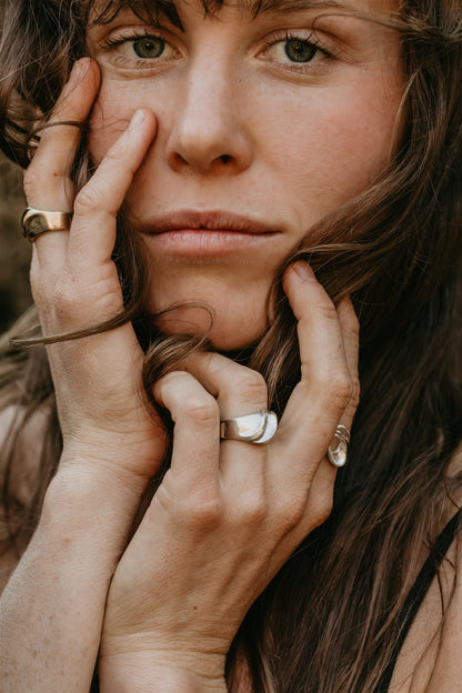 Close-up of a woman with her hands near her face, wearing rings.