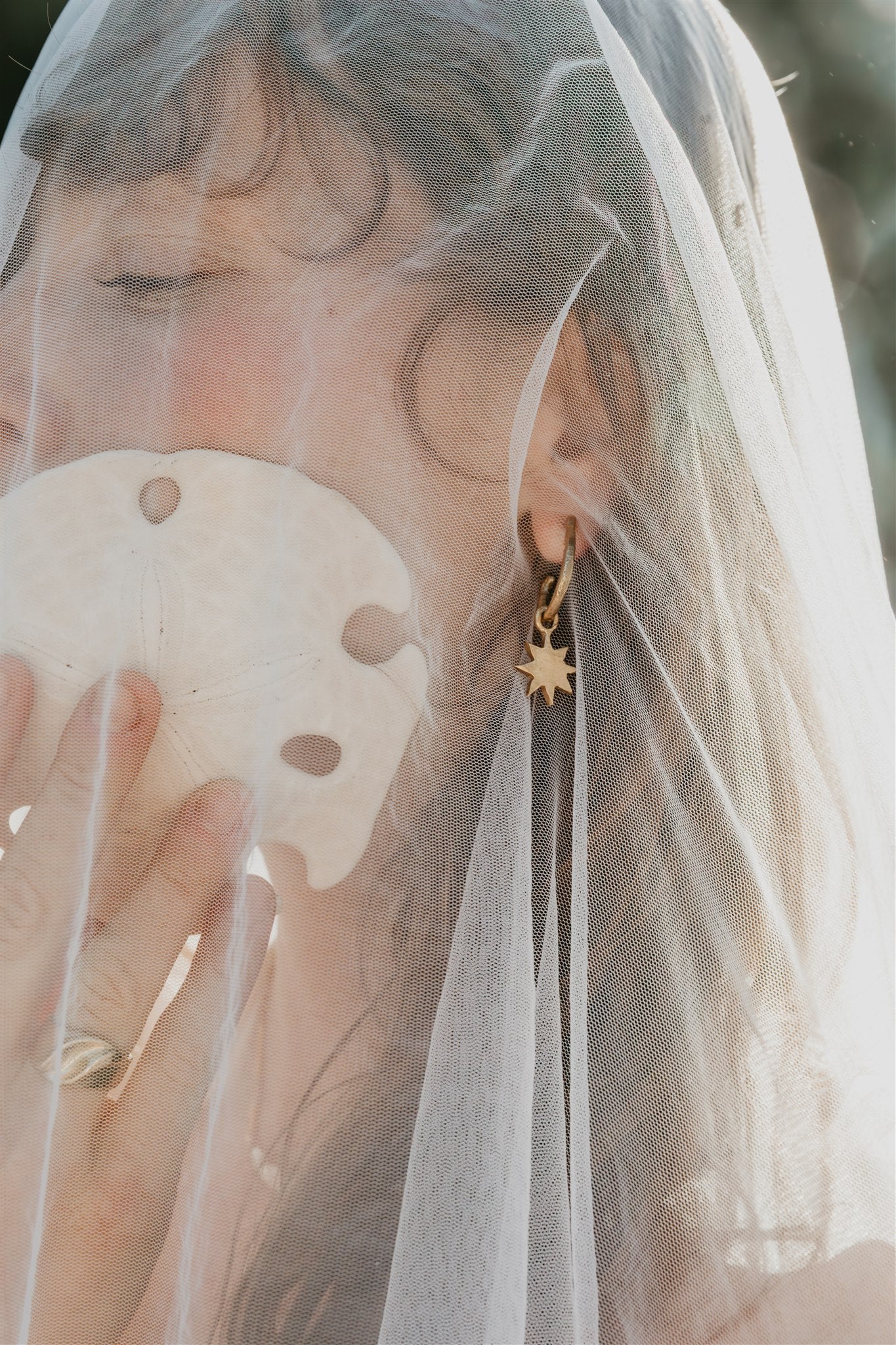 Person wearing a gold earring with a star design, holding a shell, and wearing a veil.