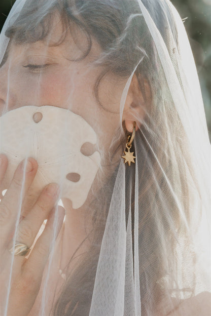 Person wearing a gold earring with a star design, holding a shell, and wearing a veil.