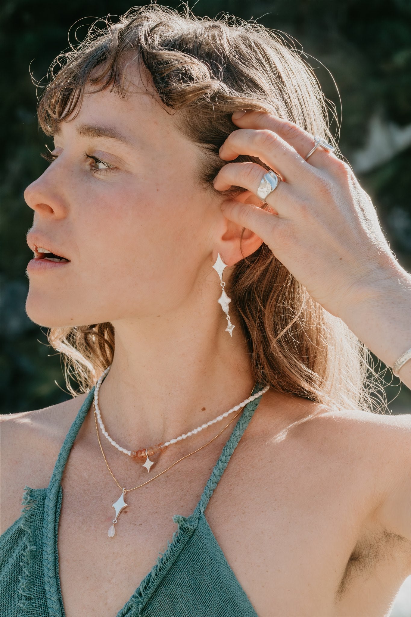 Woman wearing earrings, necklaces and a ring outdoors with a blurred natural background