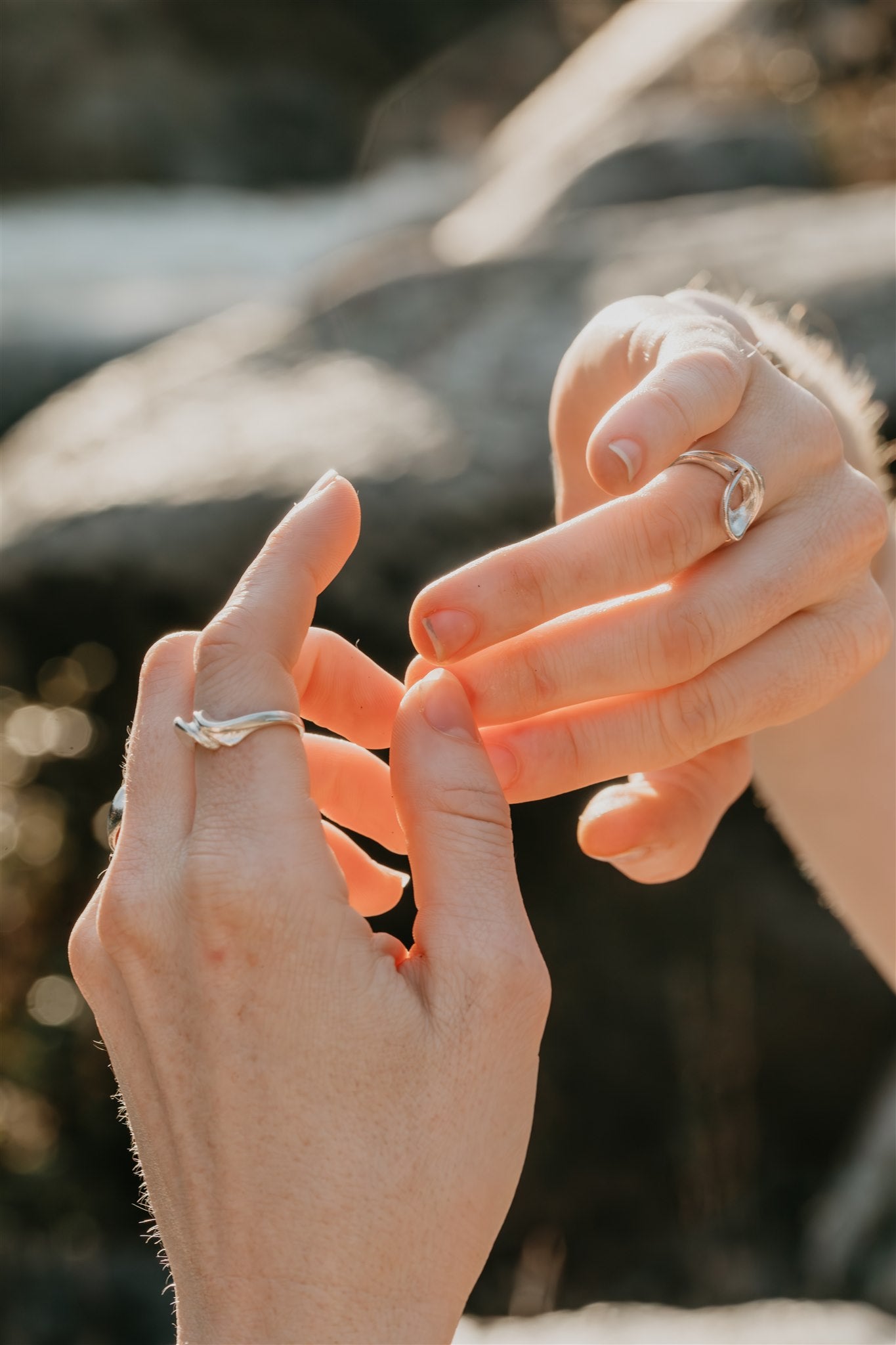 Close-up of two hands with rings on fingers against a blurred natural background