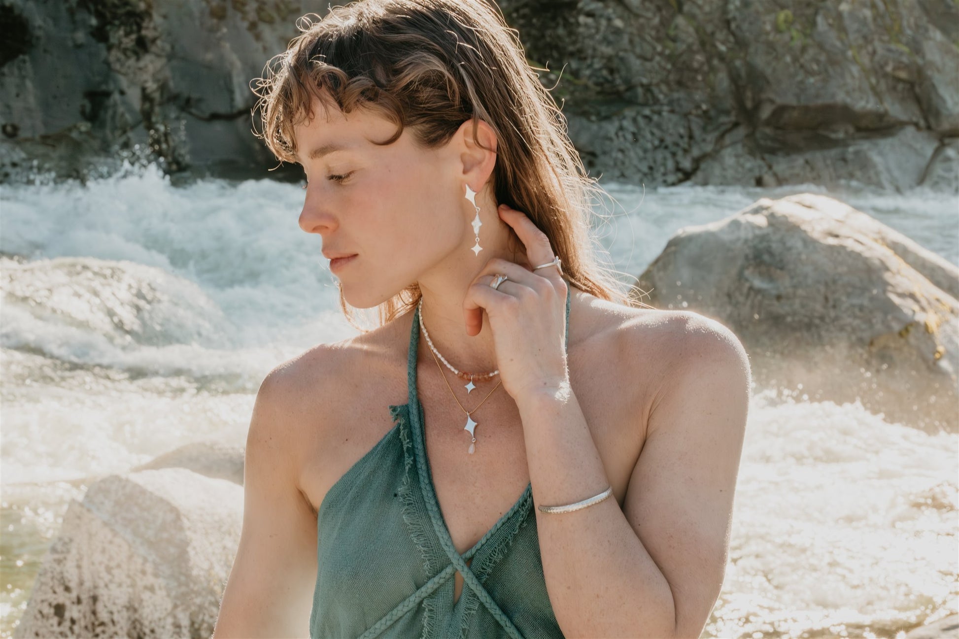 Woman wearing earrings and a necklace by a rocky water source