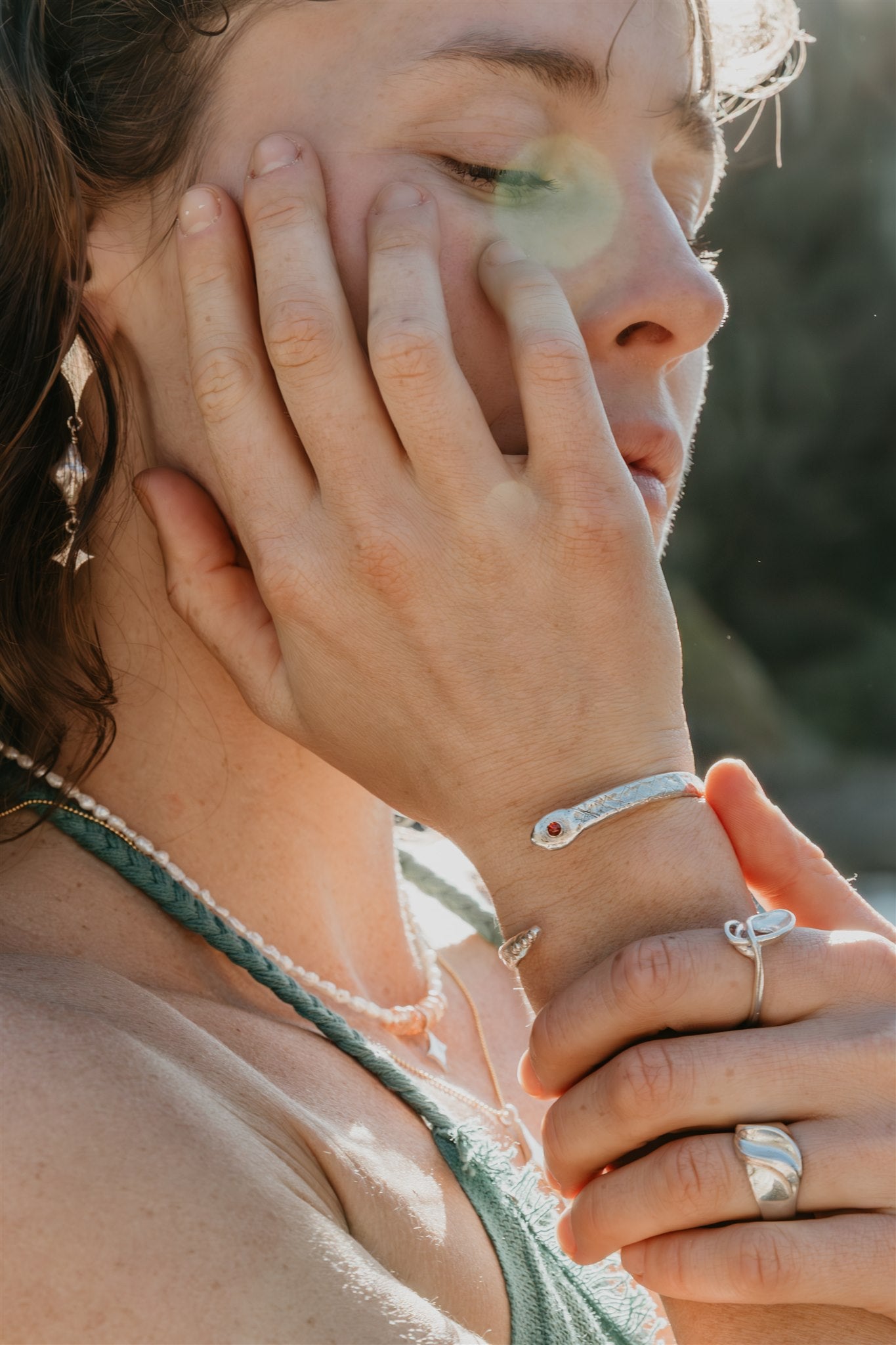 Close-up of a person with jewelry on their wrist and fingers, with a blurred natural background.