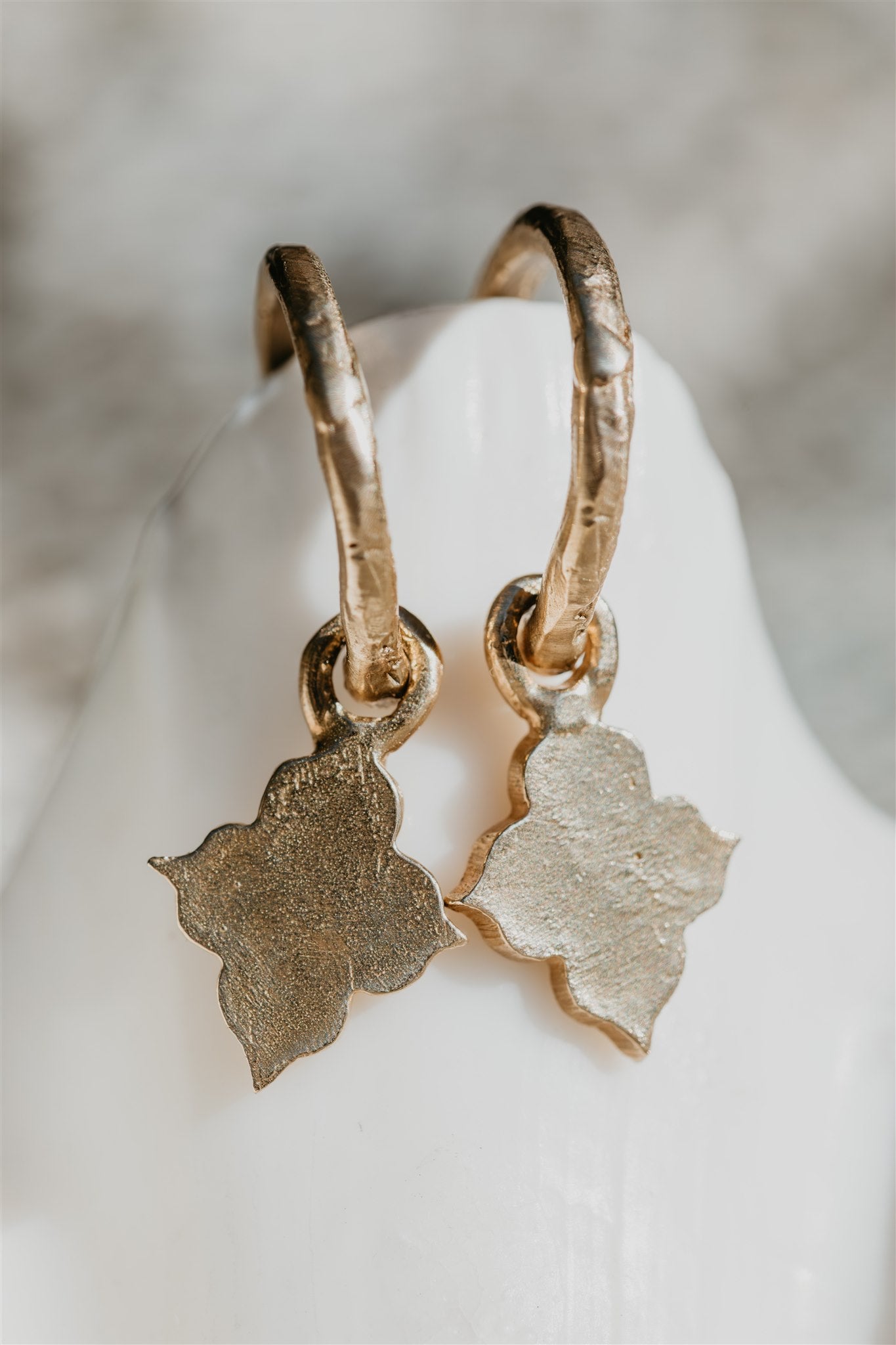 Gold hoop earrings with leaf-shaped charms on a white shell.