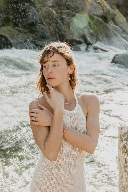 Woman in a white sleeveless dress standing by a river, wearing jewelry