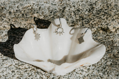 Silver earrings displayed on a white shell against a textured stone background