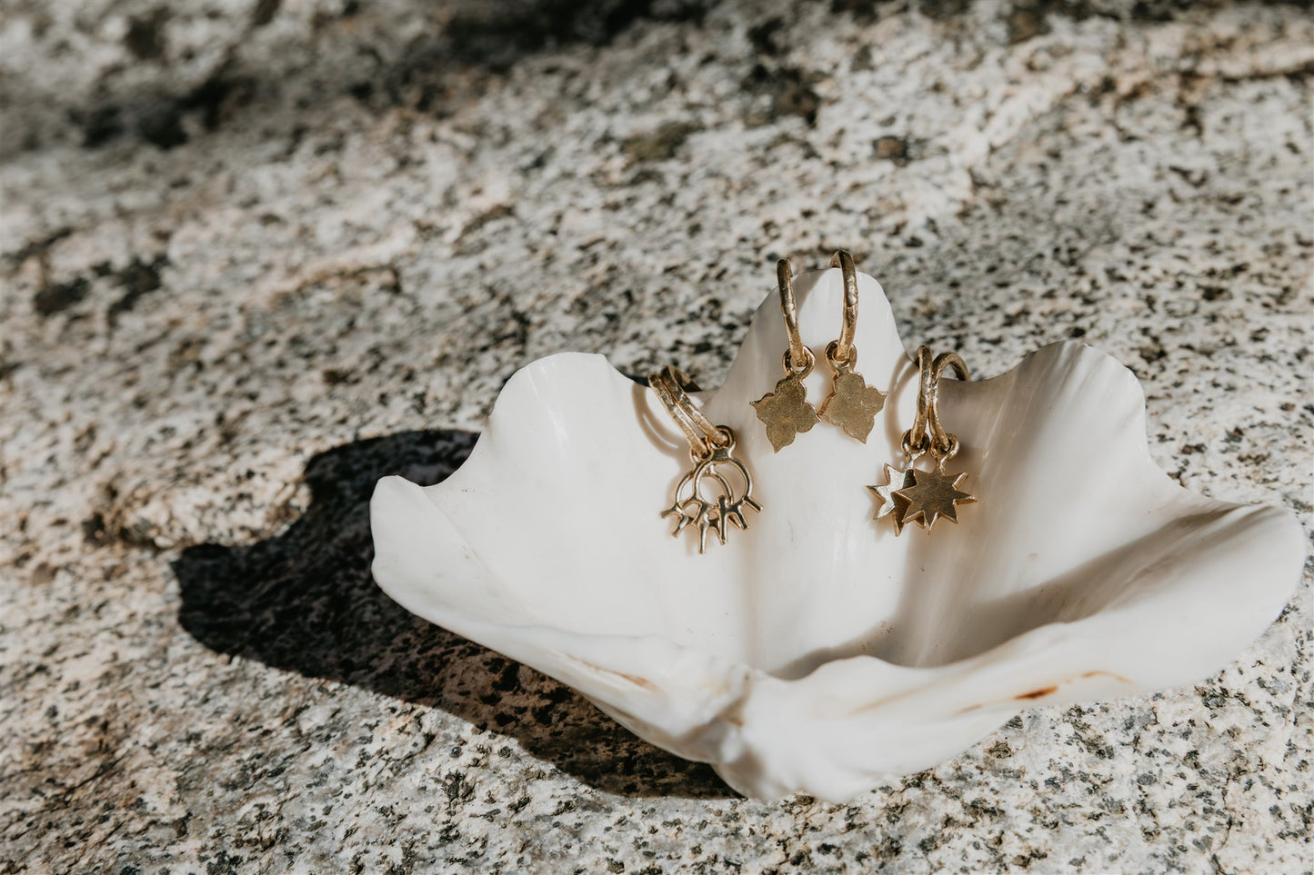 Gold earrings on a white shell against a textured stone background