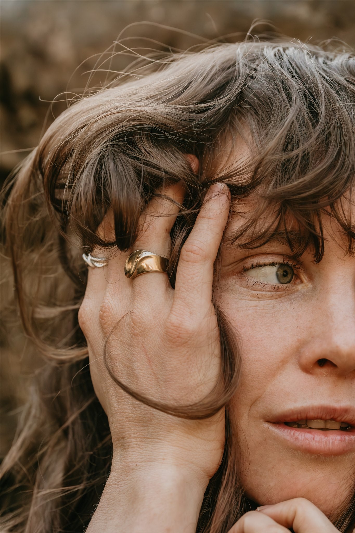 Close-up of a person with a hand on their head, wearing a gold ring.