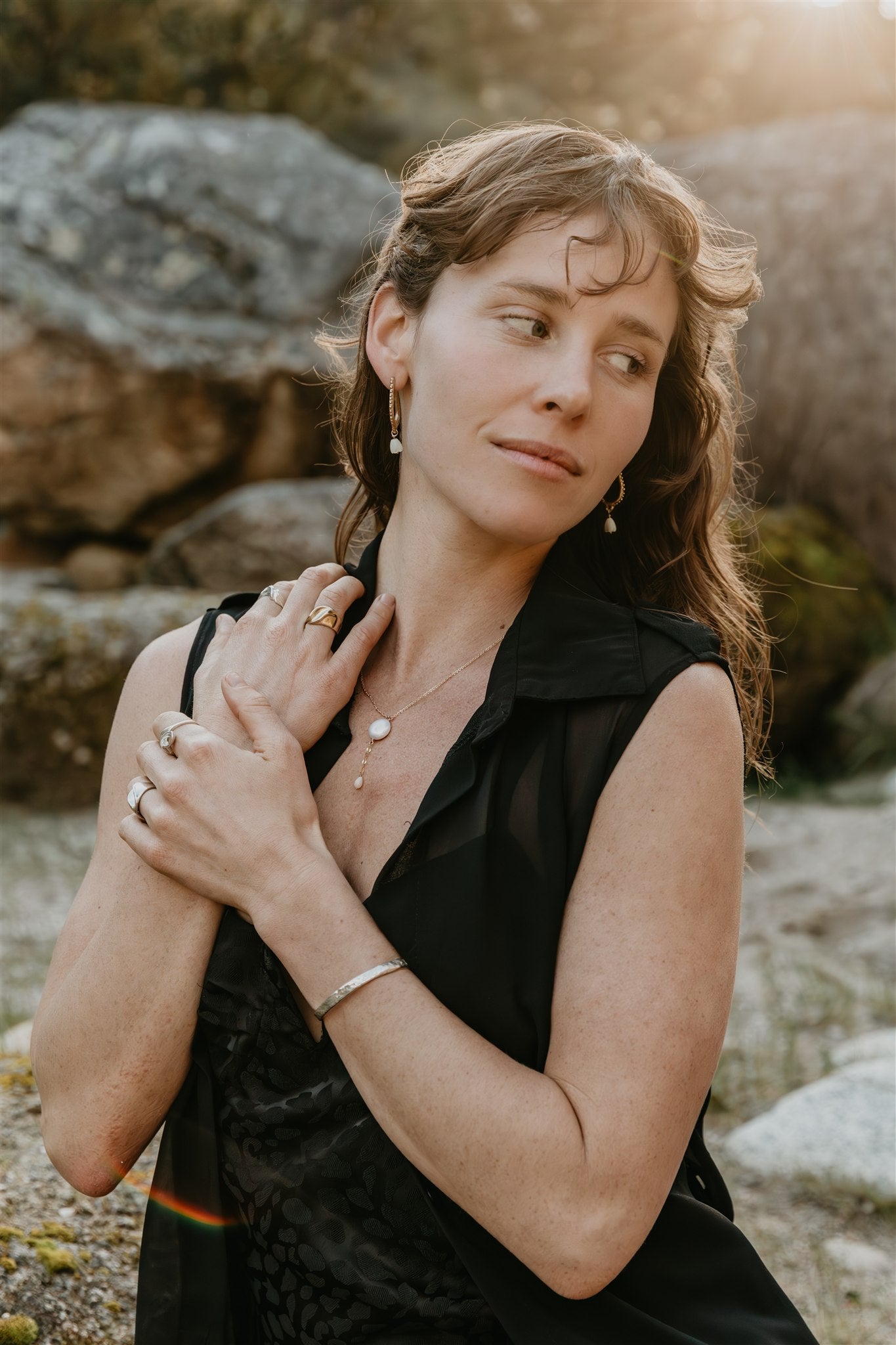 Woman in a black dress standing outdoors with rocks and natural light in the background