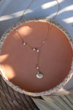 Load image into Gallery viewer, A gold lariat style necklace with lustrous pearls and a gold shell detail, displayed on a woven mat.

