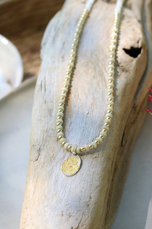Gold beaded necklace with a pendant on a piece of driftwood.