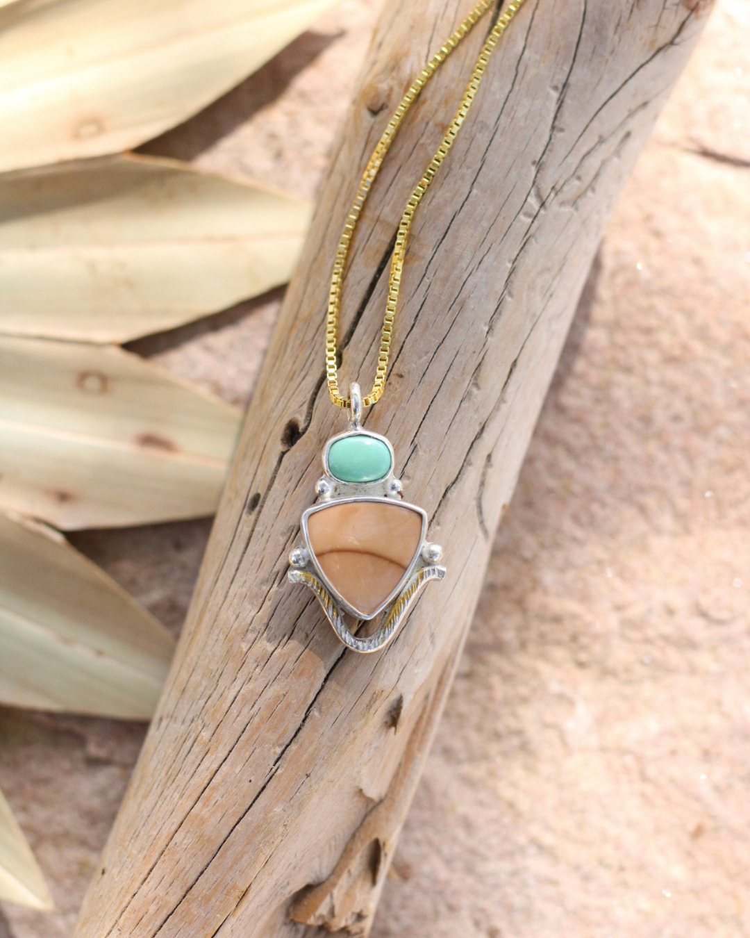 Necklace with a pendant featuring a turquoise and jasper stone on a wooden surface