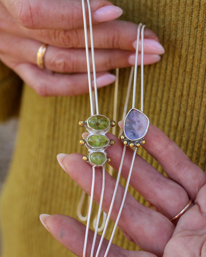 Two bolo style necklaces with gemstone pendants held by a person against a yellow background.