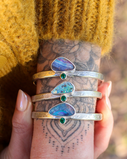 arm wearing multiple silver bracelets with opals and emerald on a blurred natural background