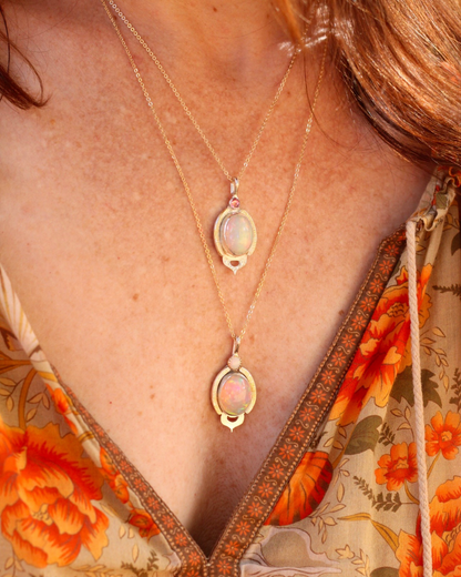 Close-up of a person wearing a gold necklace with opal pendants against a floral garment.