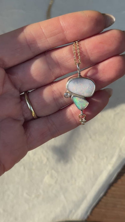 a close-up video of a person hand with an opal necklace. necklace has two opals and a moonstone, a small charm hangs below
